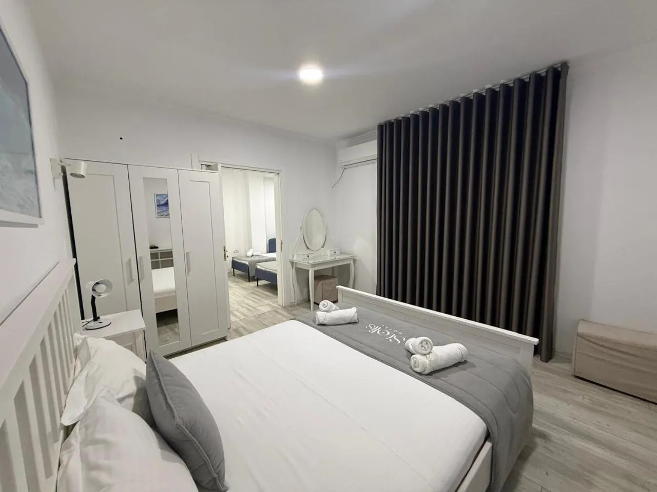 A double bed with a grey runner, a dressing table with a round mirror and long dark curtains
