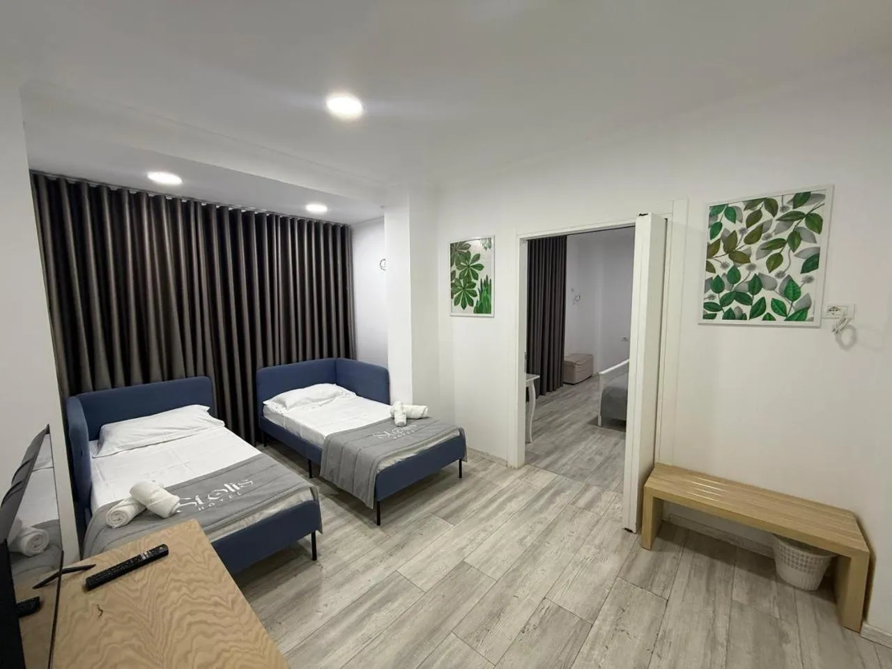 Two blue sofa beds made up with white linen, a wooden bench and a painting of green leaves