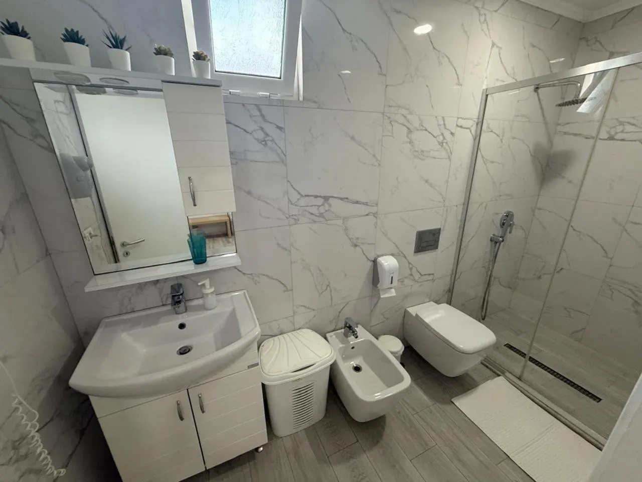 A white marble-effect bathroom with a glass shower, a toilet, a bidet and a basin
