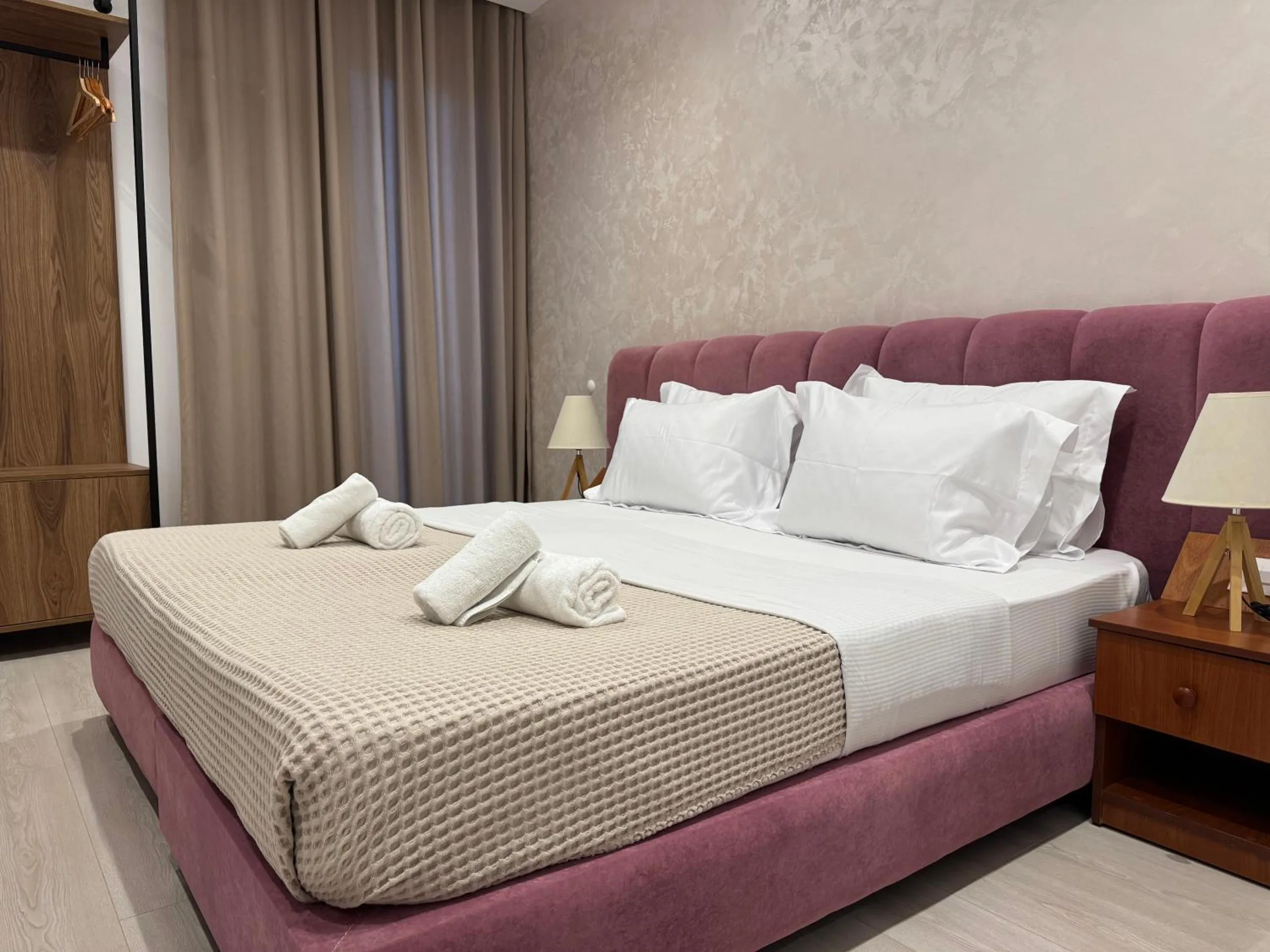 A mountain-view double at Hotel Veizi: a rose upholstered queen bed with folded towels, a bedside lamp and damask plaster