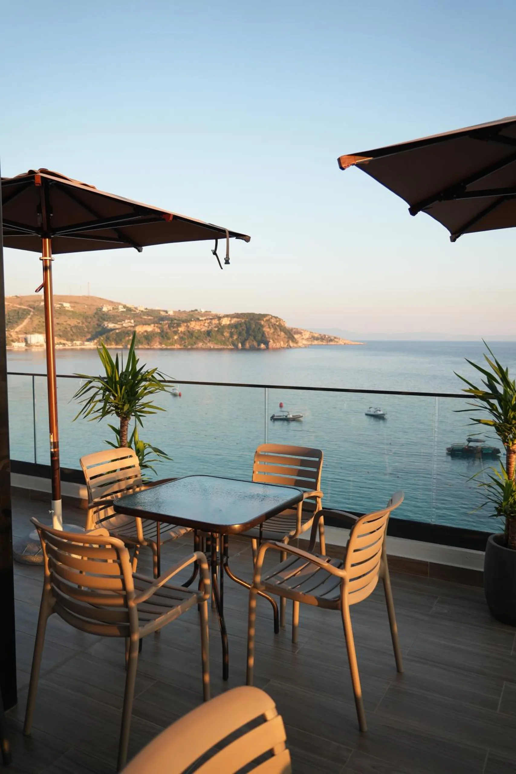 A table for two on the roof terrace in evening light, with two parasols and the bay and its headland beyond the rail