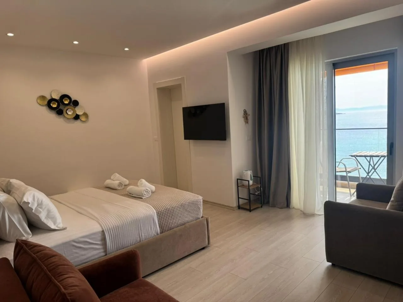 A sea-view double at Hotel Veizi: a made-up double bed, a grey sofa and the balcony door with the sea beyond