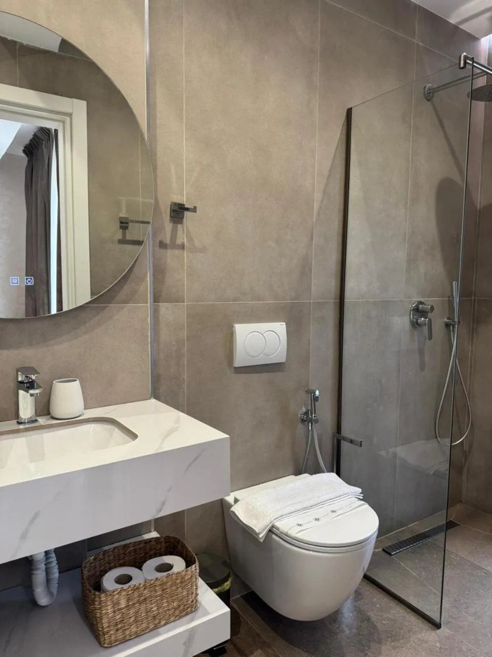 The shower room of a sea-view double: a glass shower, a round mirror and a marble basin