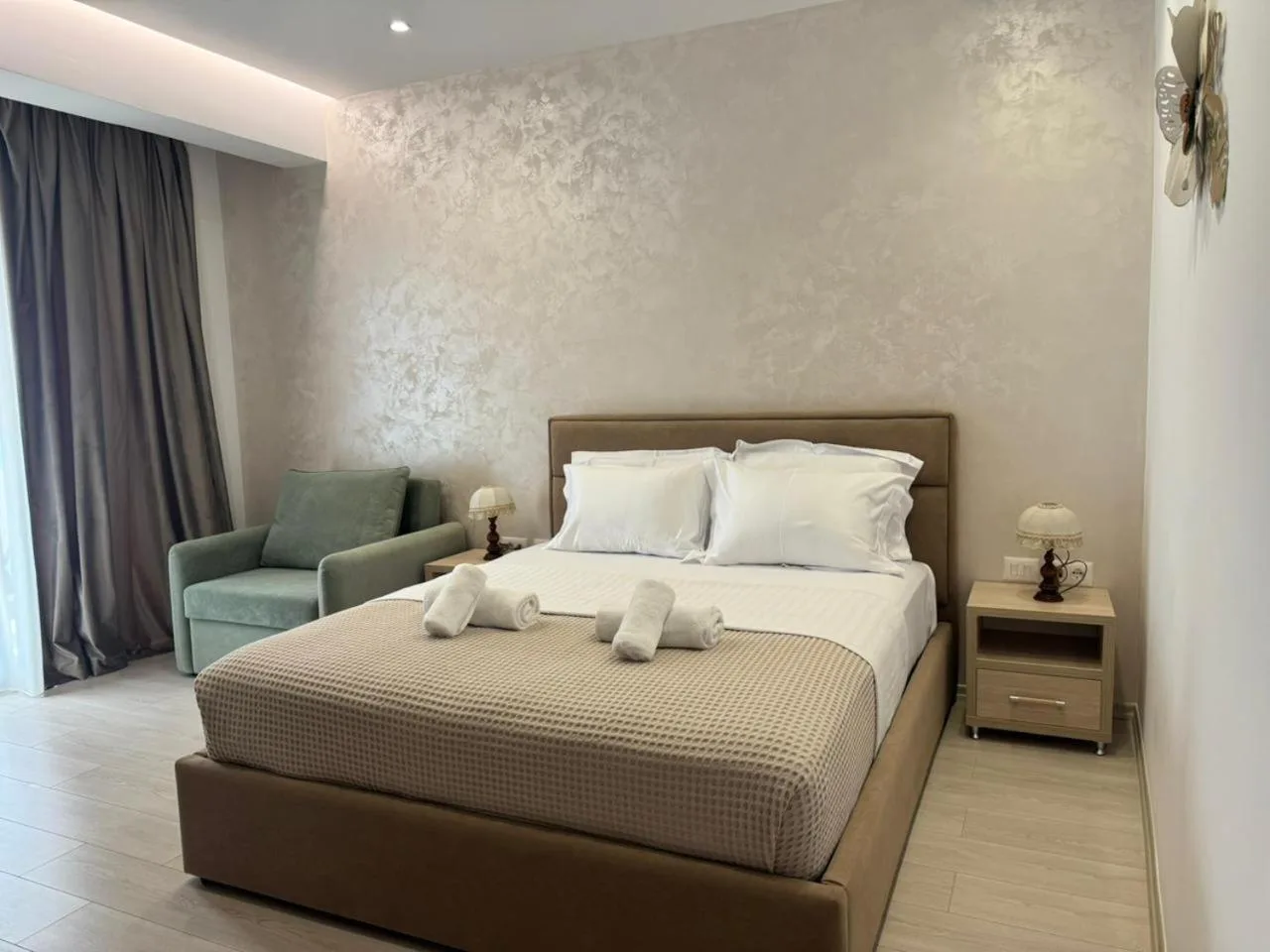 A sea-view double with a queen bed, a green armchair, a bedside lamp and damask plaster behind the headboard
