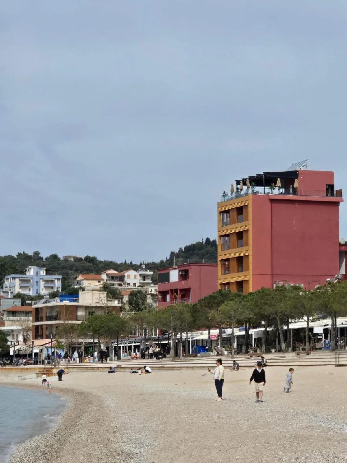 Hotel Veizi seen from the shingle of Spile beach, standing over the pines of the promenade