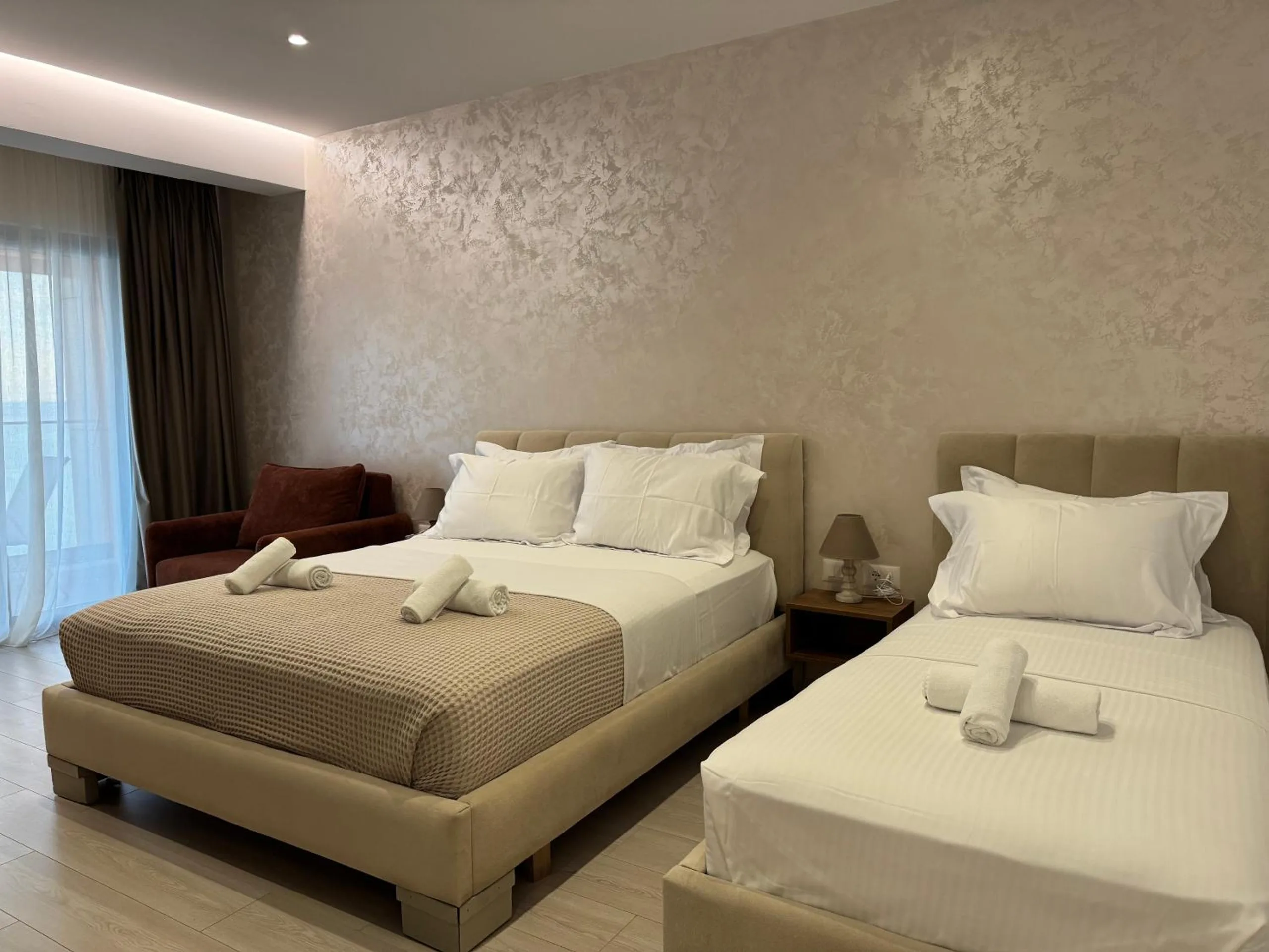 A sea-view triple at Hotel Veizi: a queen bed and a single bed side by side, a rust-coloured sofa and the balcony curtains
