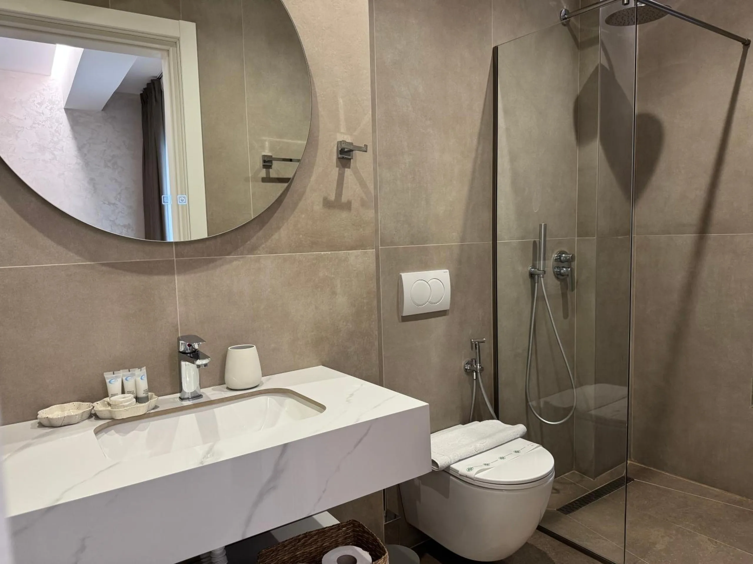 The shower room of a sea-view triple: a round mirror over a marble basin and a glass shower