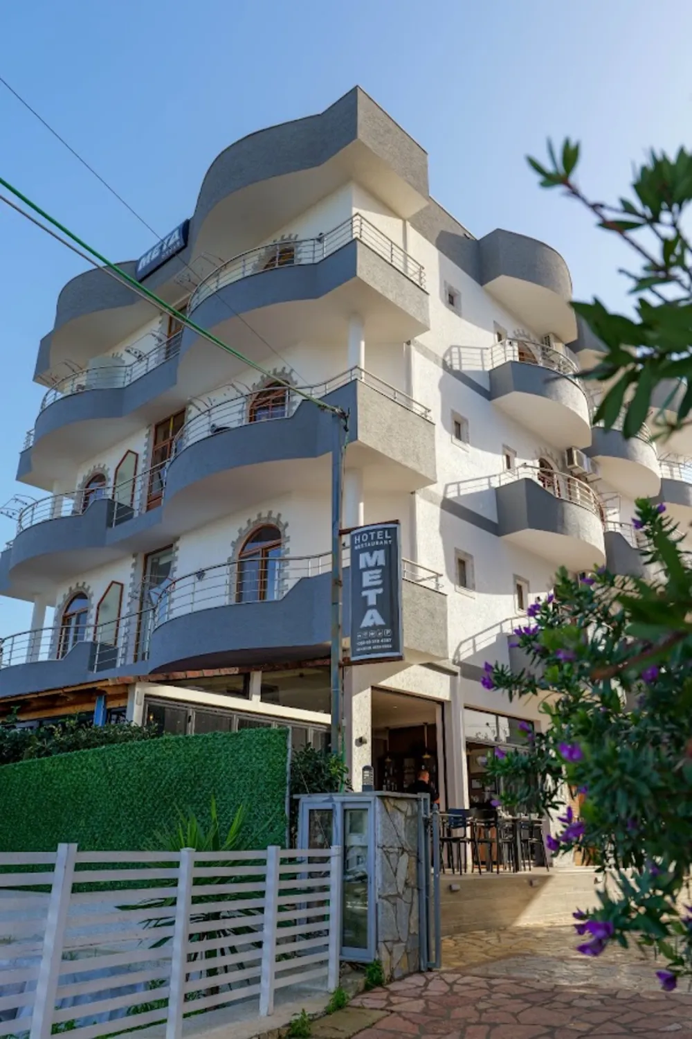 Hotel Meta in Ksamil, a white four-storey hotel with curved balconies and a vertical name sign above the entrance