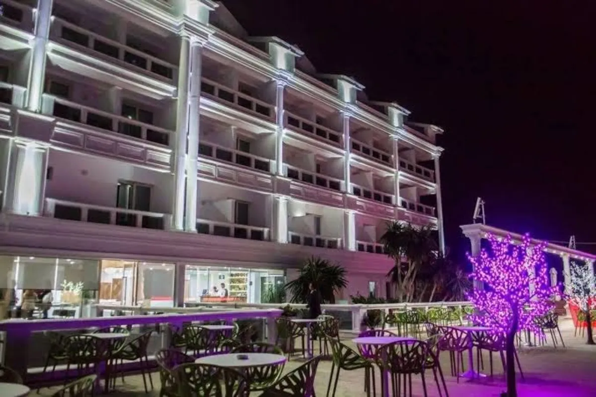 Santa Quaranta Premium Resort in Saranda at night, a white multi-storey hotel lit up above a terrace with cherry-blossom style lights