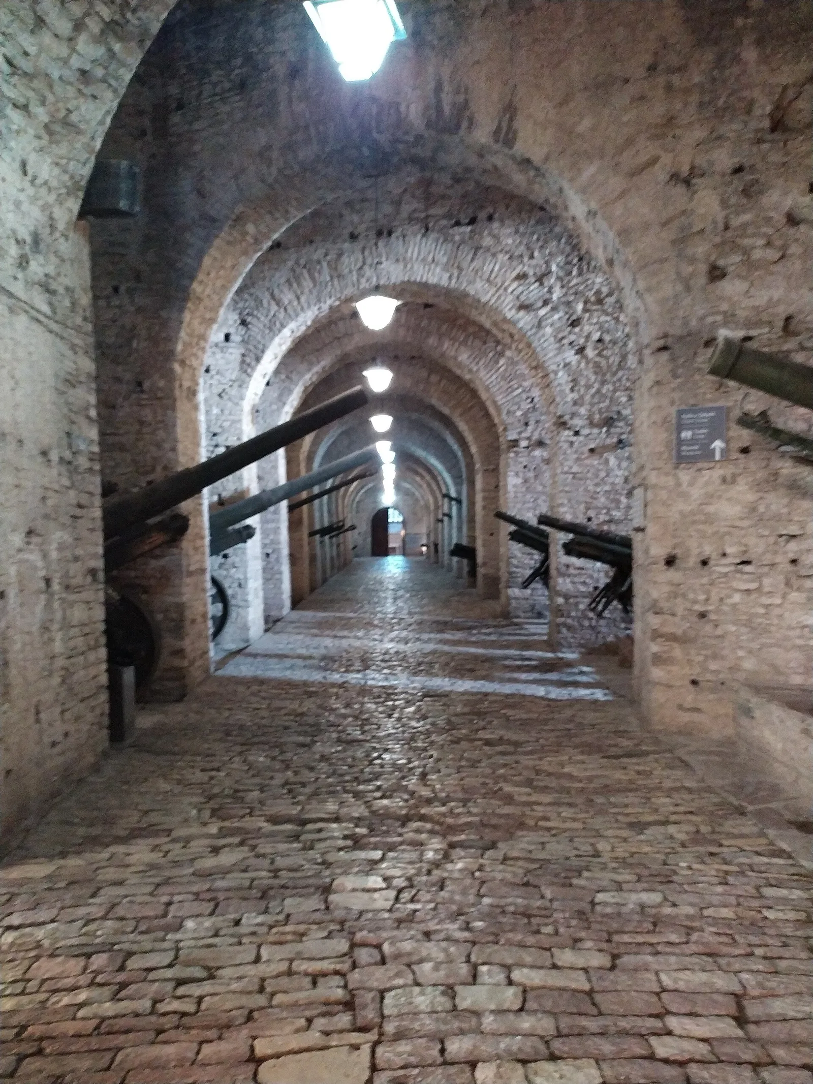 Long vaulted stone gallery with a cobbled floor, artillery pieces lined up under the arches on both sides