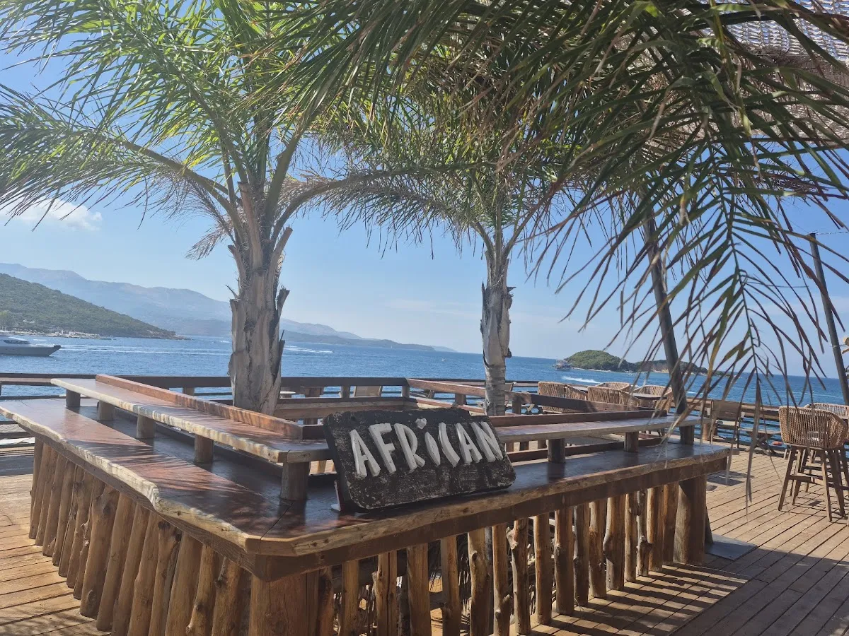 The bar at Africana Beach Club in Ksamil, a timber counter under palm trees looking out over the sea and an islet