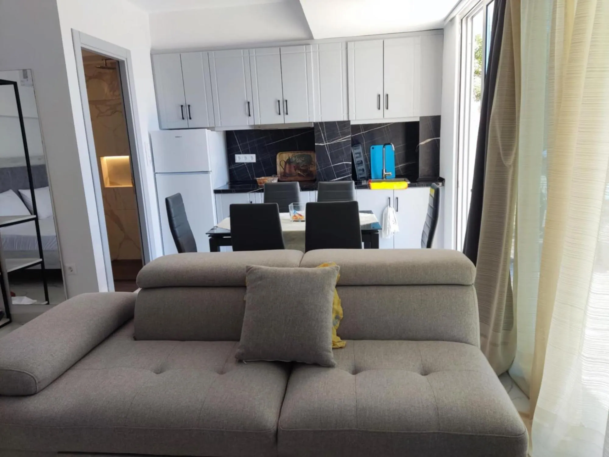 A unit at Ionian Pearl with a grey sofa in front of a dining table and a fitted kitchen with white cupboards and a fridge
