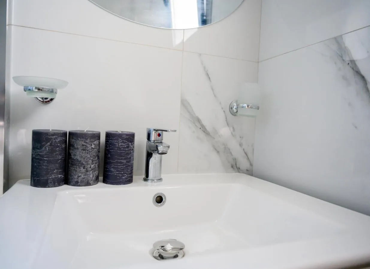 A white bathtub against marble-effect tiles at Ionian Pearl, with three grey candles on its rim and a chrome tap