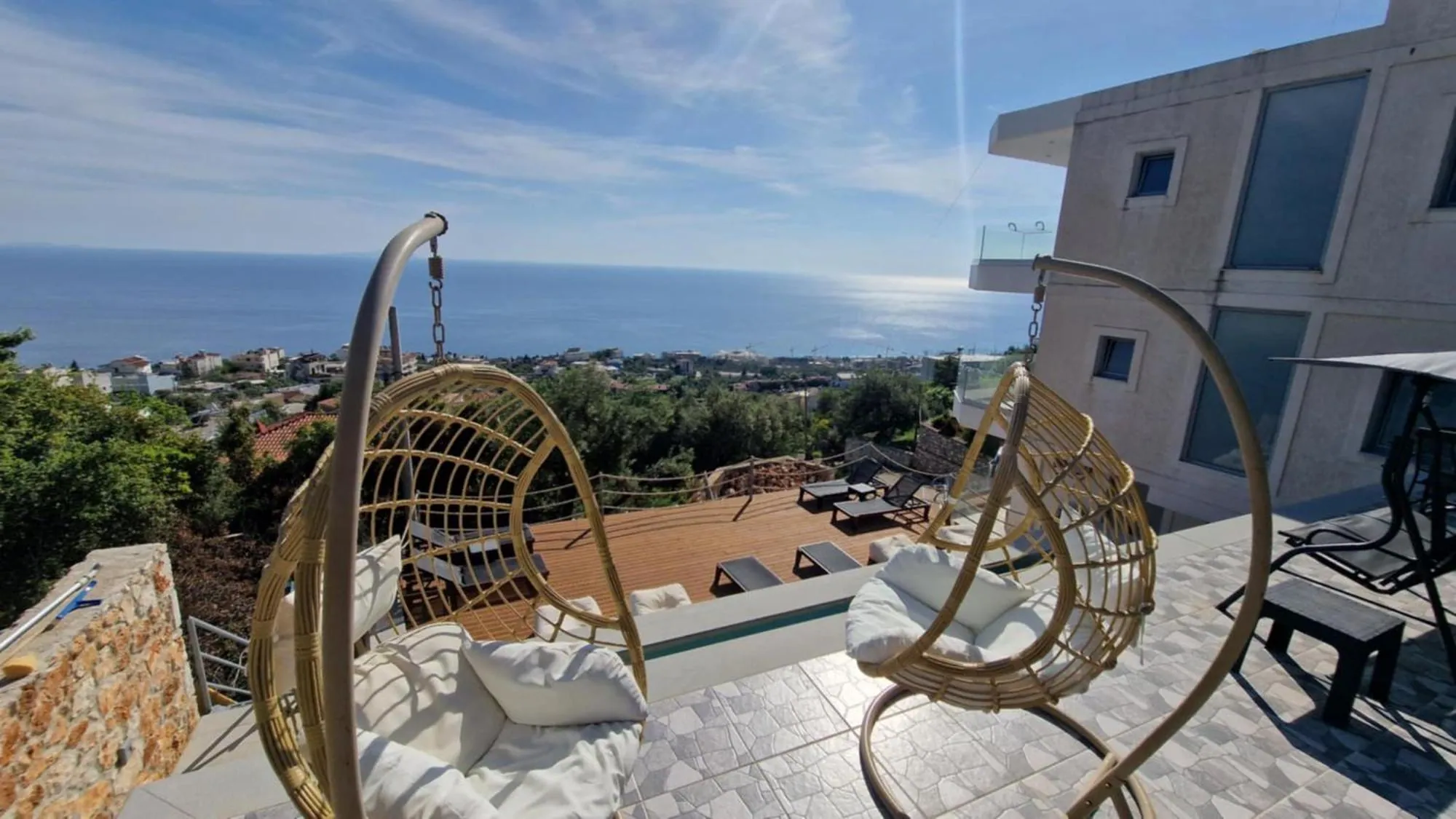 Two rattan egg chairs hanging on the kitchen terrace at Ionian Pearl, looking down over the pool deck to the coast and the sea