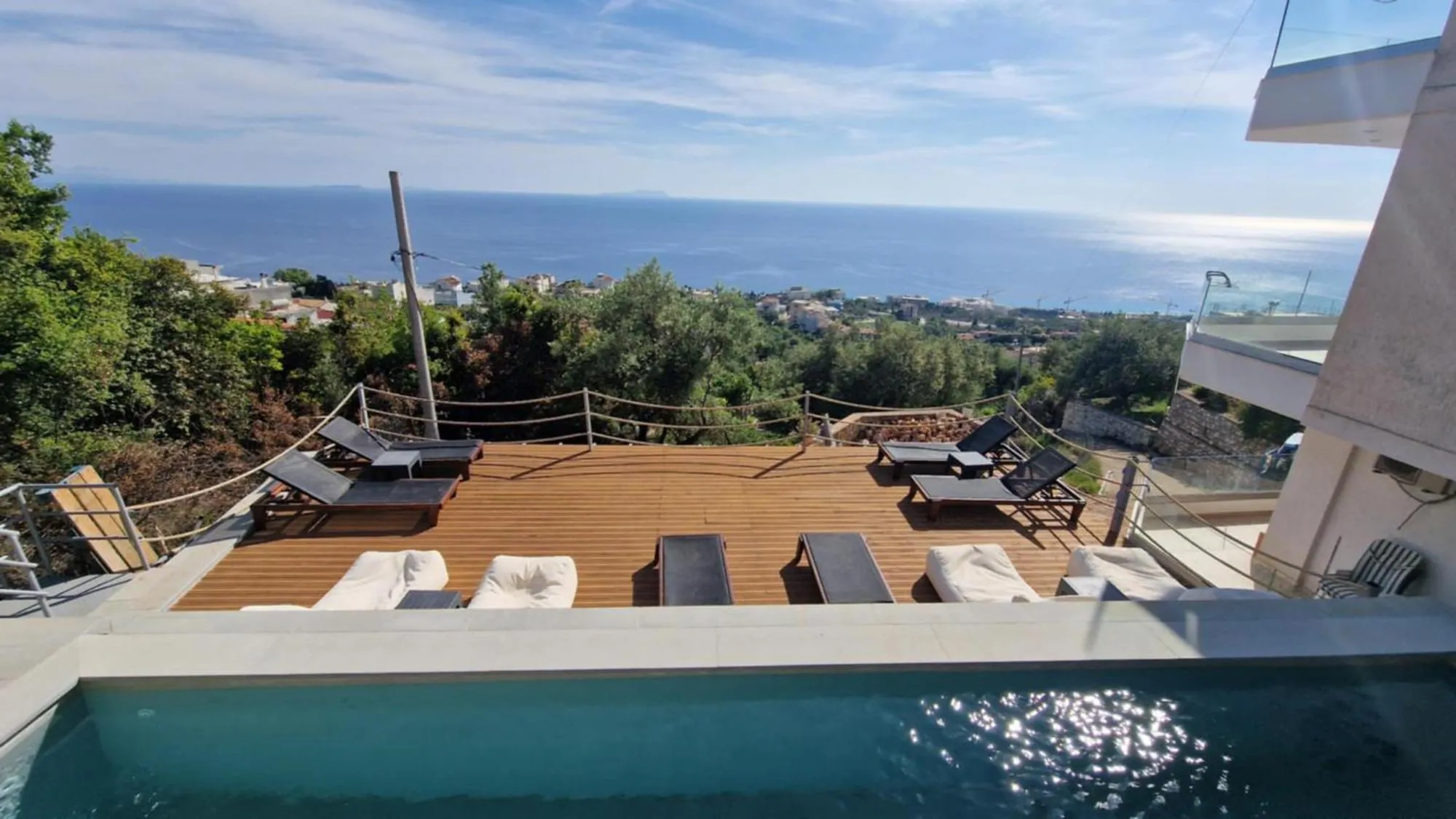 The edge of the pool at Ionian Pearl with light on the water, the deck below it and the bay of Drymades on the horizon