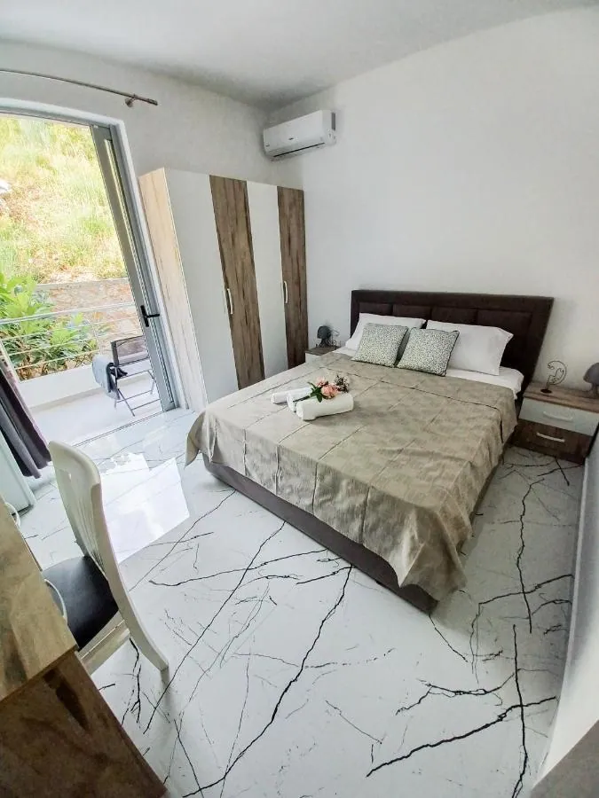 A double bed in a room at Ionian Pearl with its balcony door open onto the green slope of the mountain behind the house