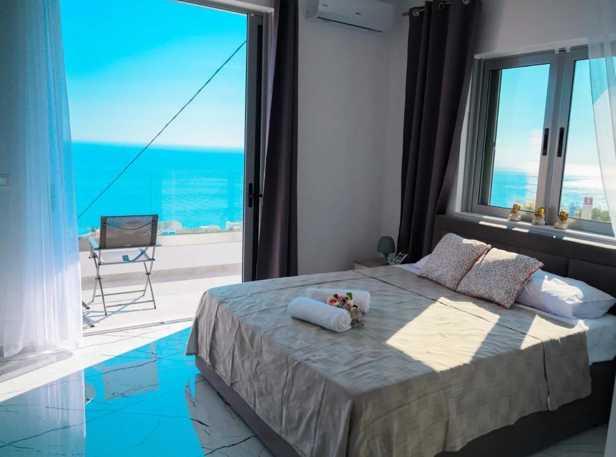 Sun on the white marble-effect floor of a double room at Ionian Pearl, with the balcony door open on a table, two chairs and the sea