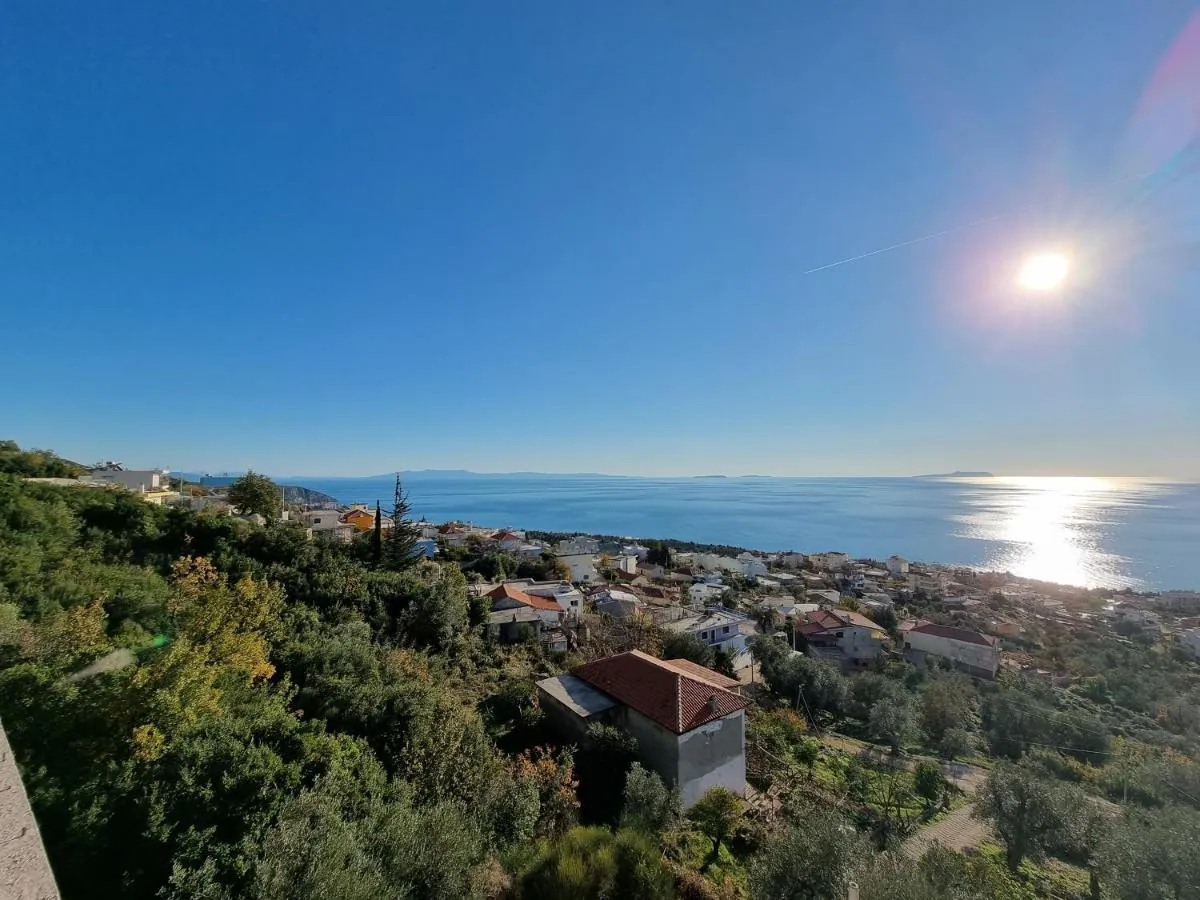 The sun low over the sea seen from the hillside at Ionian Pearl, with olive trees and village houses in the foreground and light on the water
