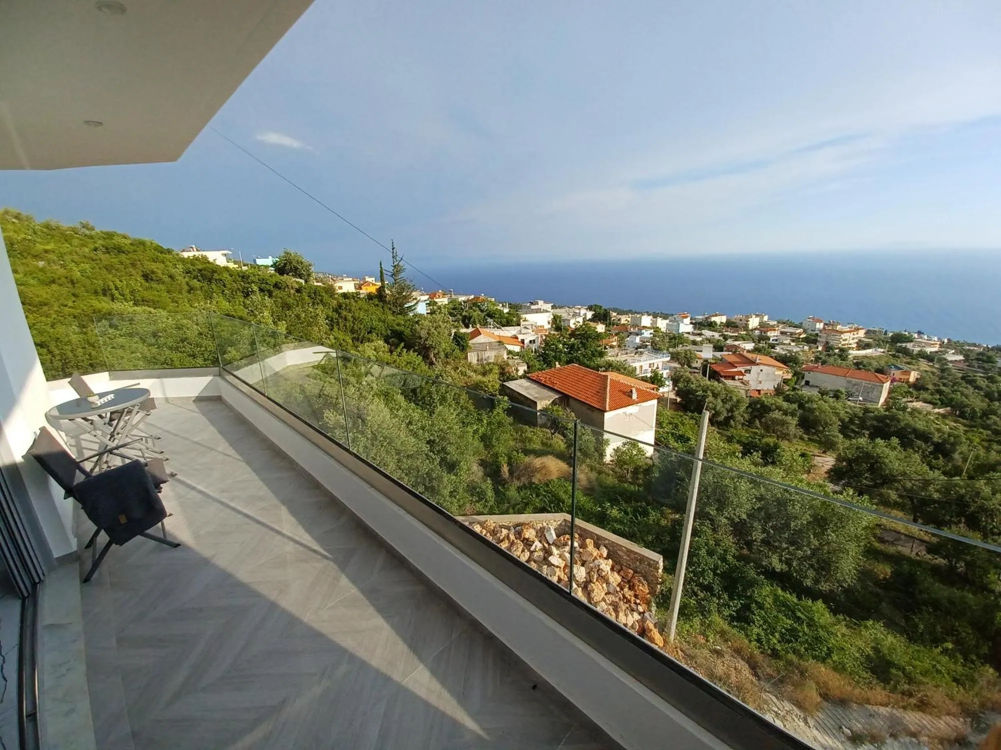 A long balcony at Ionian Pearl behind a glass balustrade, looking out over olive trees and the red roofs of the village to the sea