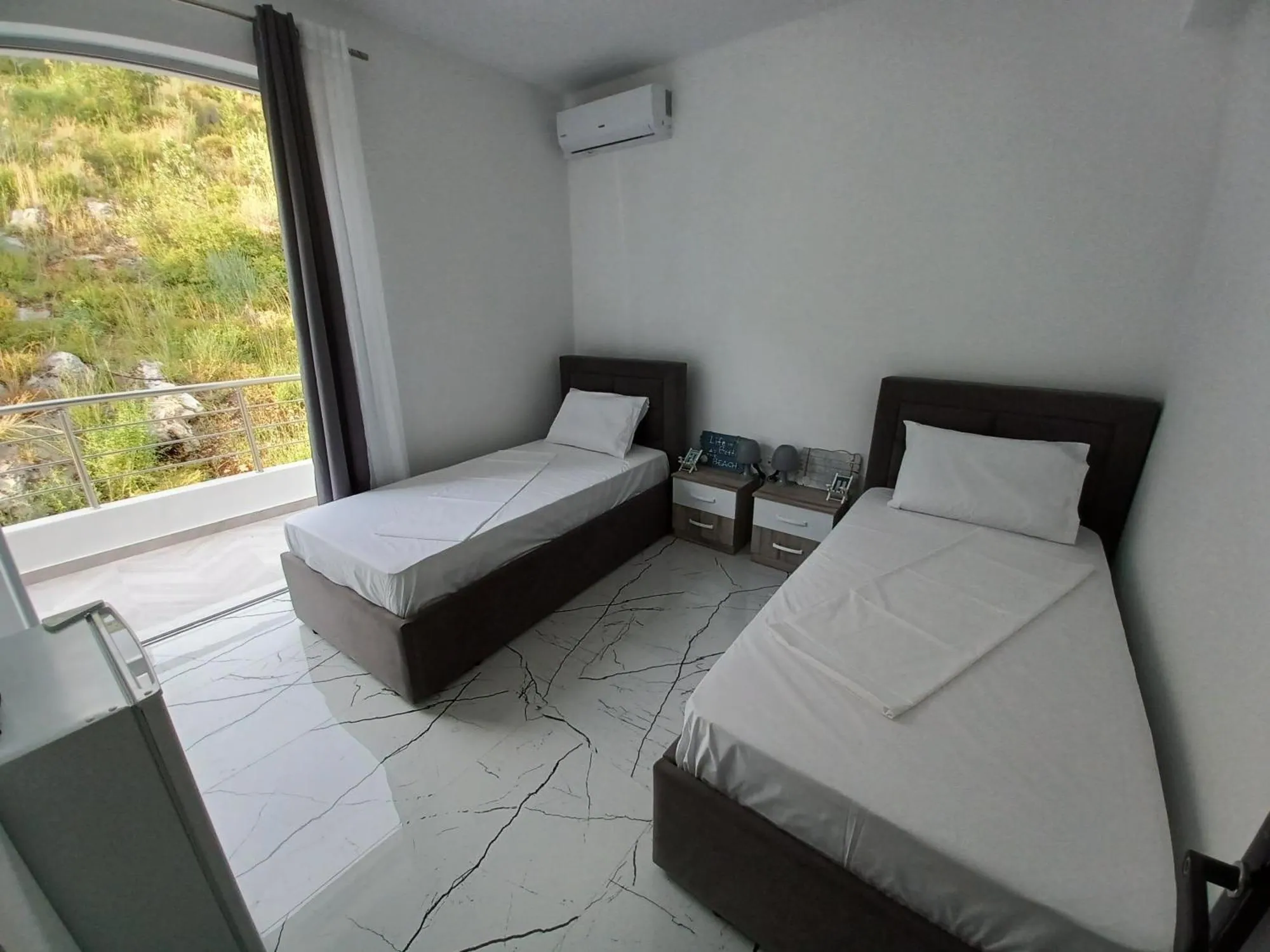 Two single beds in a white room at Ionian Pearl, with a window onto the green hillside behind the house