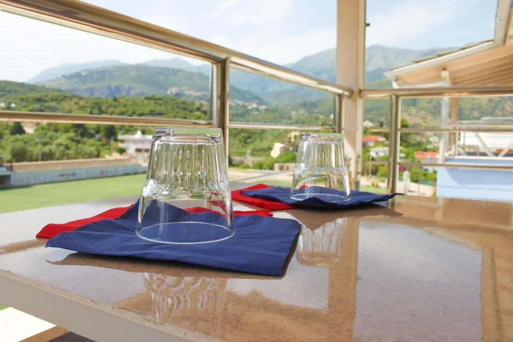 Two upturned glasses on blue napkins on a balcony table, the green pitch of the stadium below the glass rail and the mountains behind