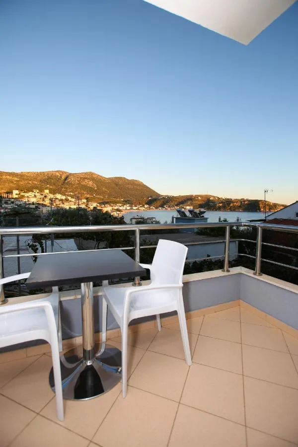 A balcony table and two white chairs in evening light, the bay and the hillside town beyond the steel rail