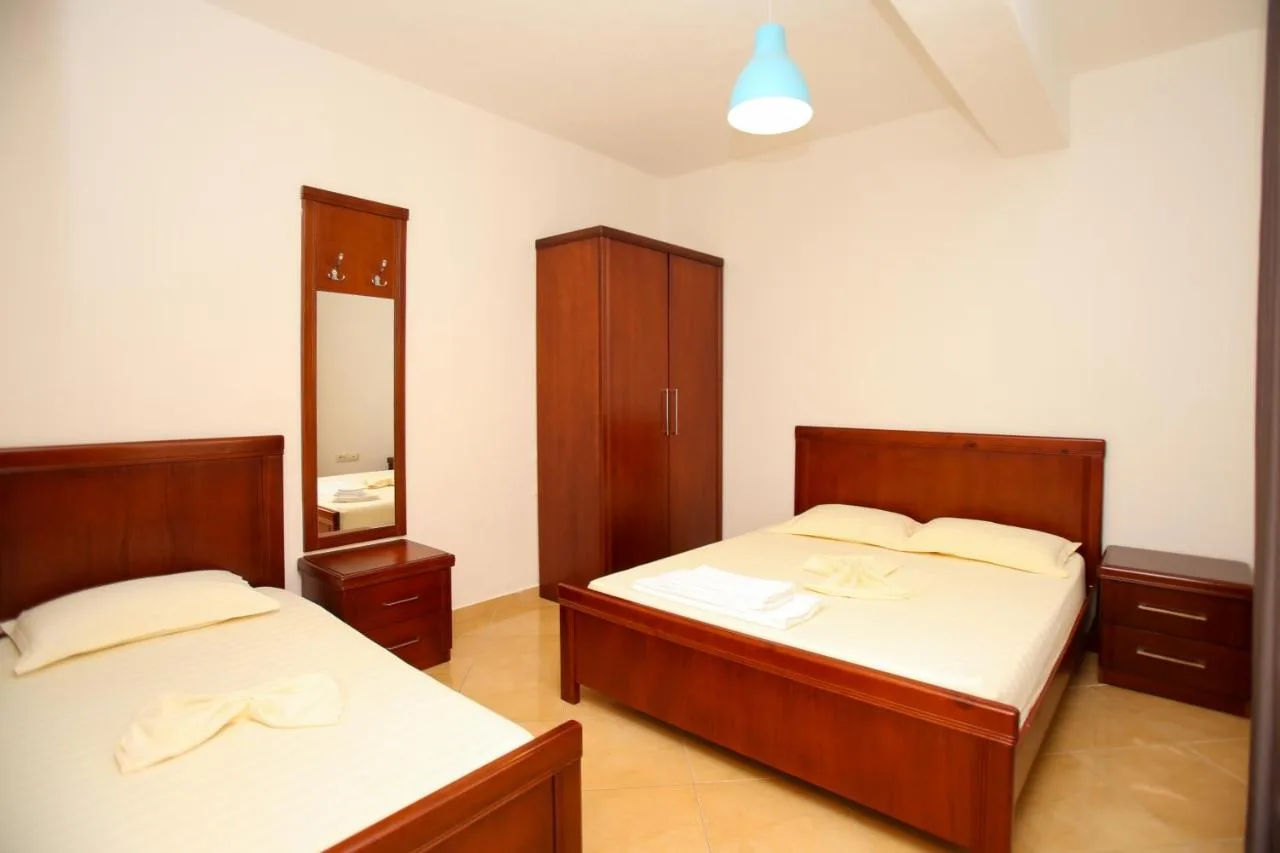 A bedroom with a double bed and a single bed in matching cherry-wood frames, a tall wardrobe and a wall mirror between them