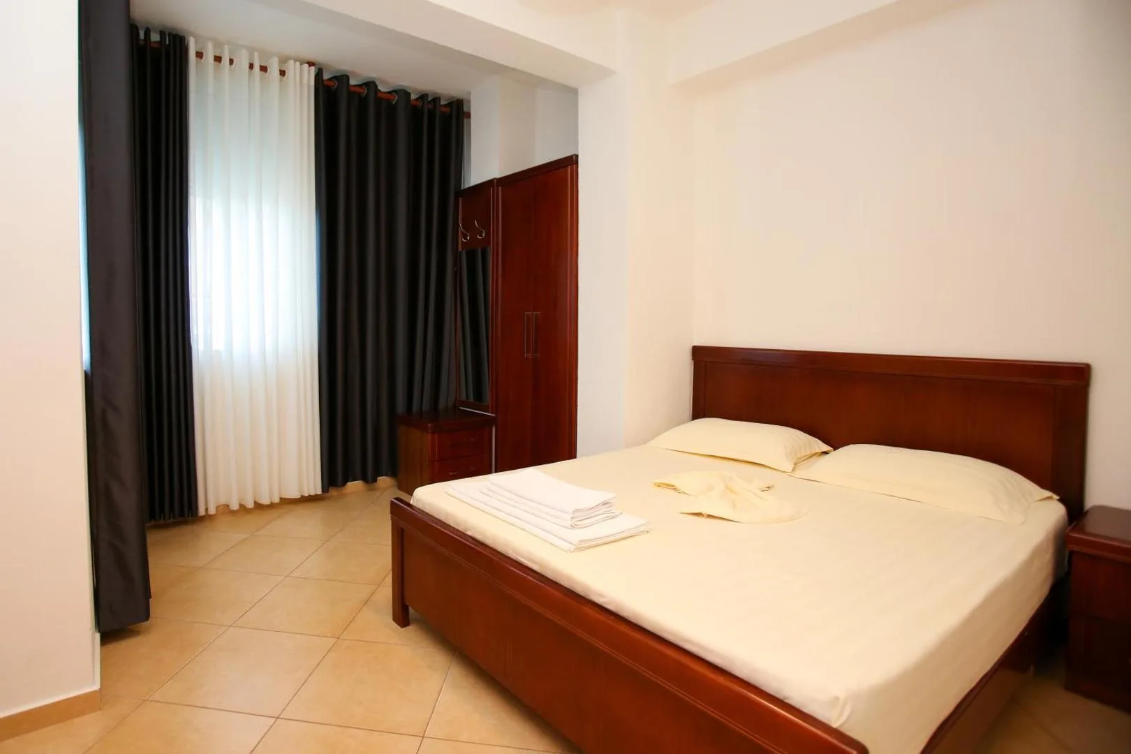 A bedroom with a large double bed in cherry-wood, towels folded on the cream sheets, a matching wardrobe and dark curtains over the window