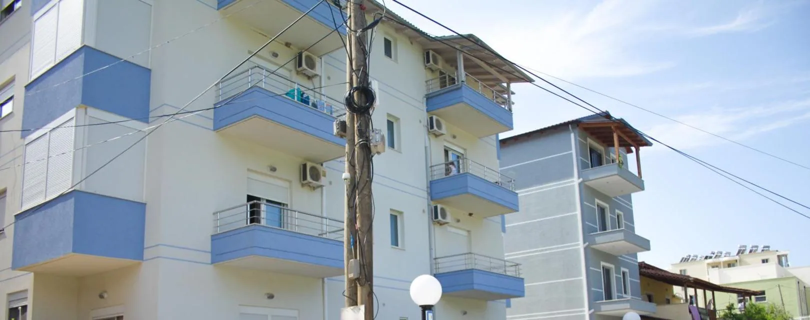 The white façade of the building with balconies faced in pale blue and thin blue lines running across the render between the floors