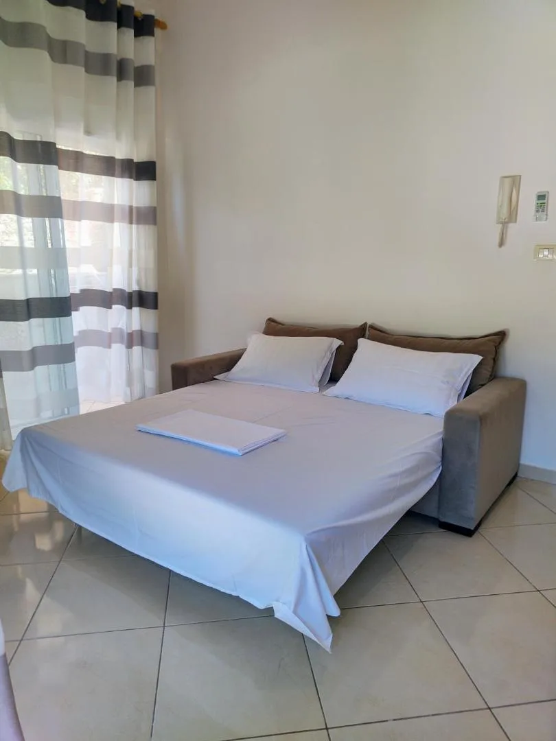 A sofa bed opened out and made up with white sheets and two pillows beside a striped curtain