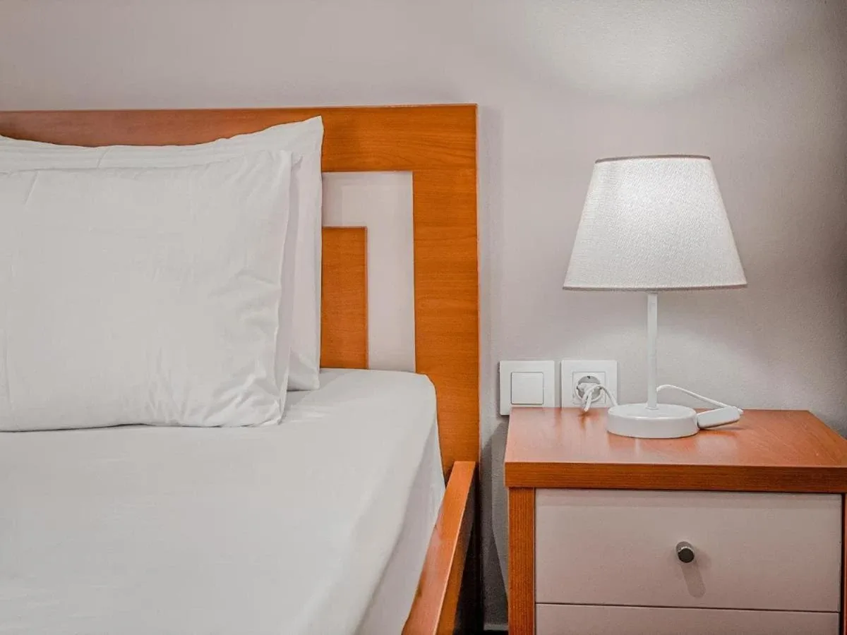 A bedside table, lamp and power sockets beside a wooden headboard at Kleanthi's Hotel