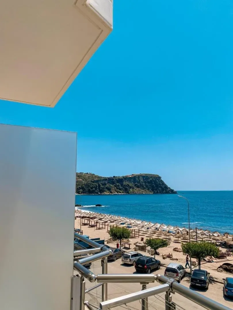 The view from a balcony at Kleanthi's Hotel past a frosted privacy screen to Prinos Beach, its straw parasols and the headland beyond