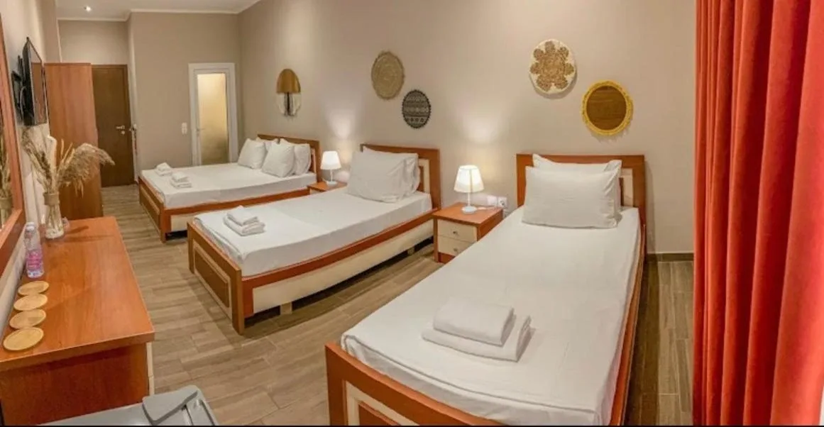 A room at Kleanthi's Hotel with three beds, bedside lamps and a red curtain at the balcony door