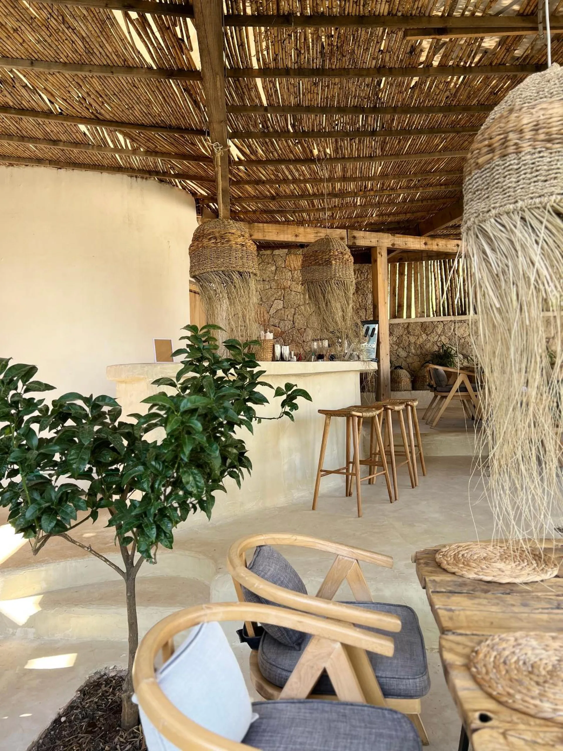 Jute pendant lamps hanging over wooden bar stools and a small potted tree on the terrace