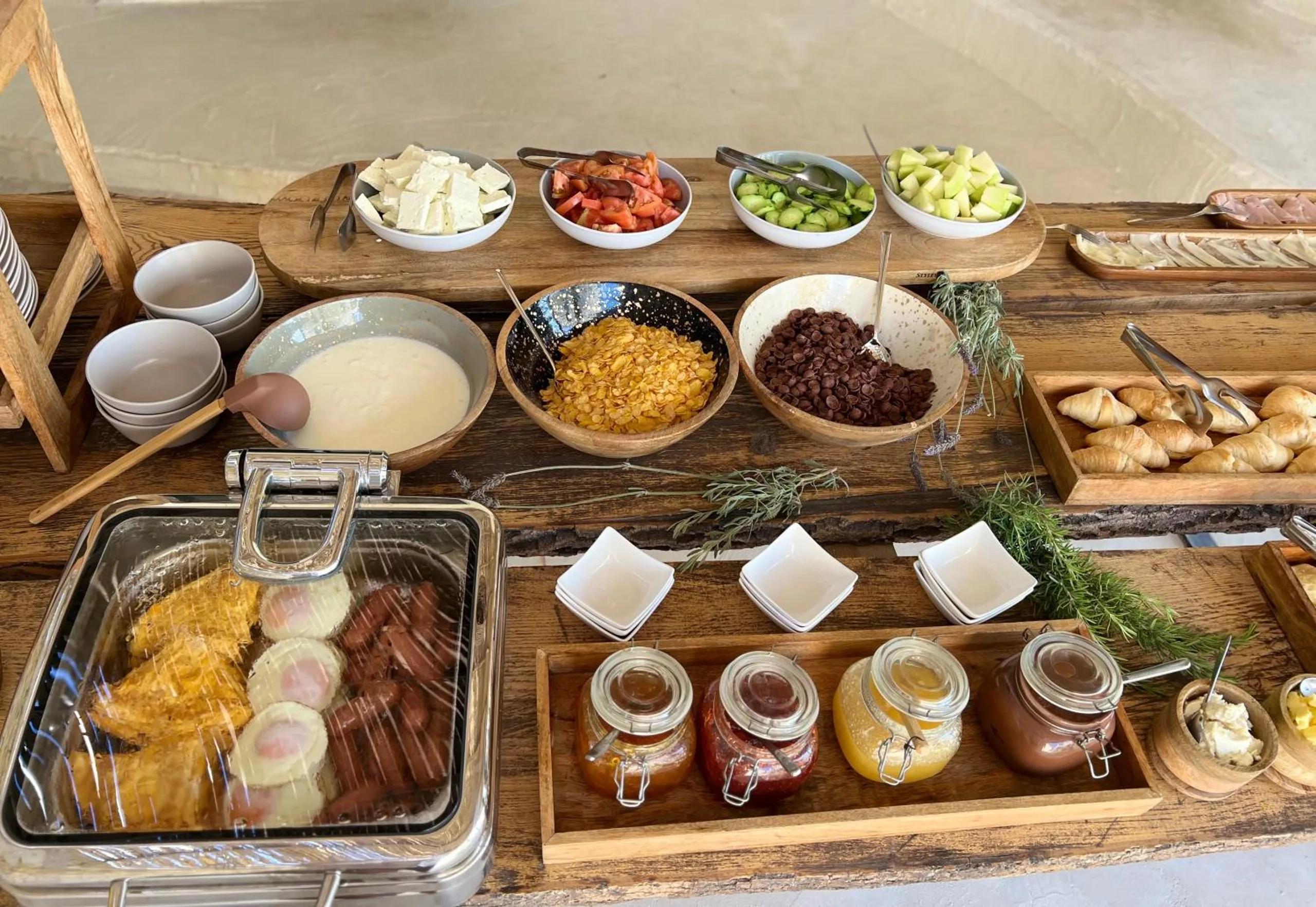 Breakfast laid on timber boards: a chafing dish of eggs and sausages, bowls of semolina, cereal and dried fruit, and jars of jam