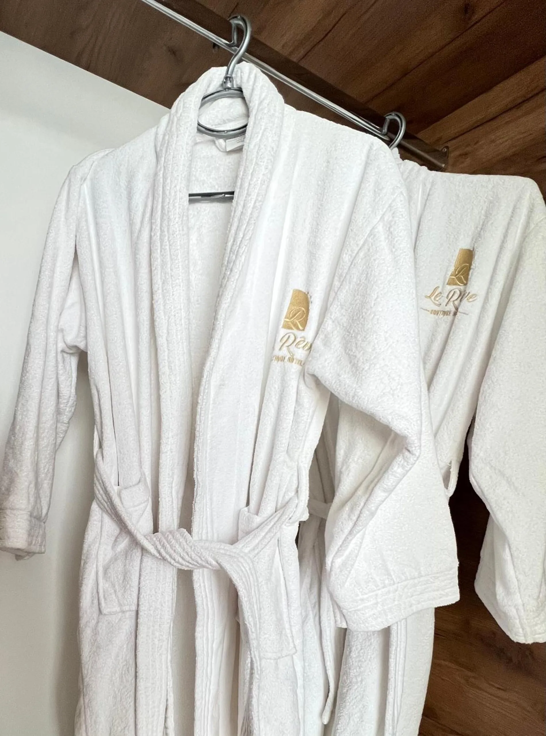 Two white bathrobes on a rail, each embroidered in gold with the hotel's R mark and the words Le Rêve