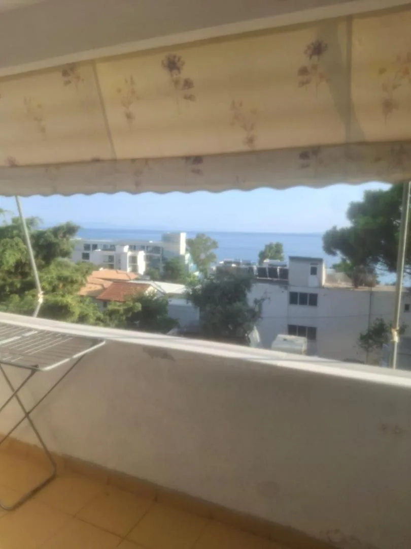 The view from a balcony under a cream awning printed with lilac flowers: pines, red-tile roofs and the sea beyond