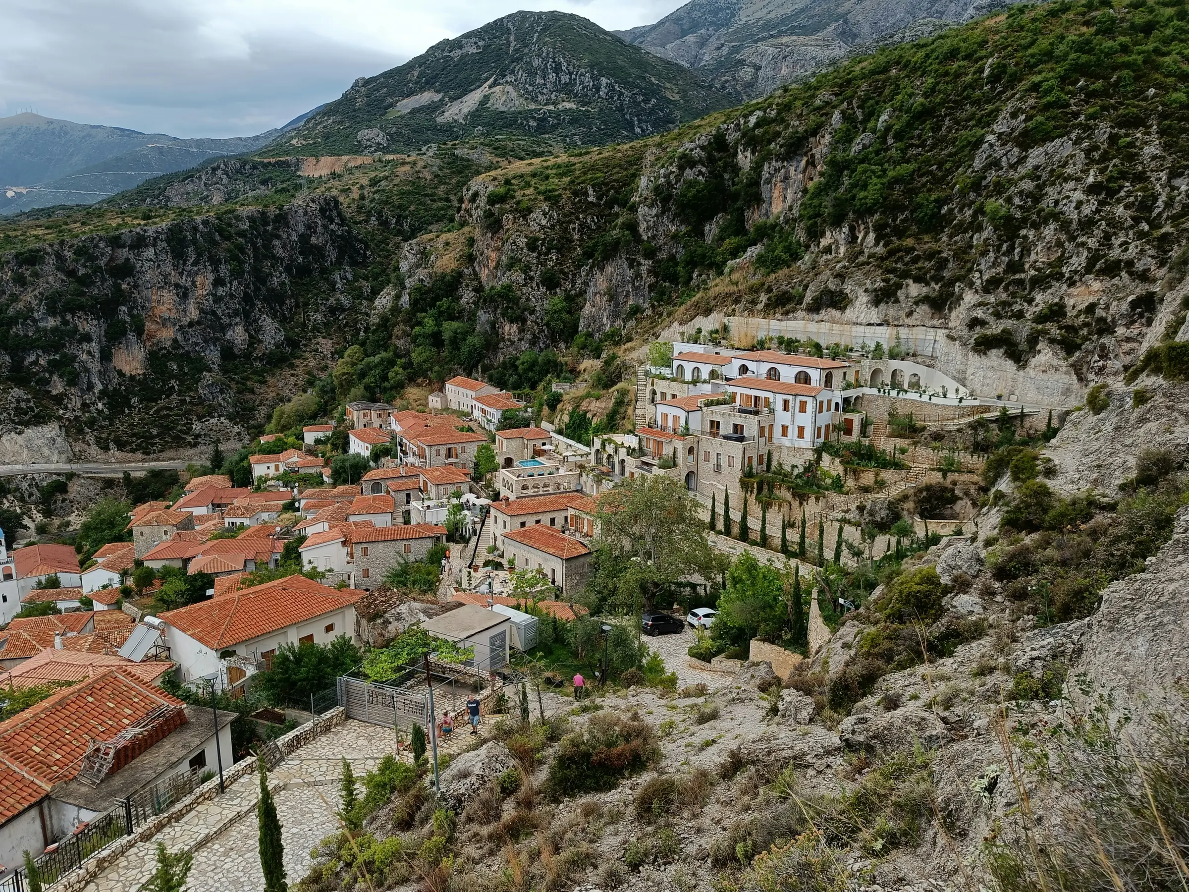 Stone houses with red-tile roofs stepping up the slope of old Dhërmi under grey limestone peaks