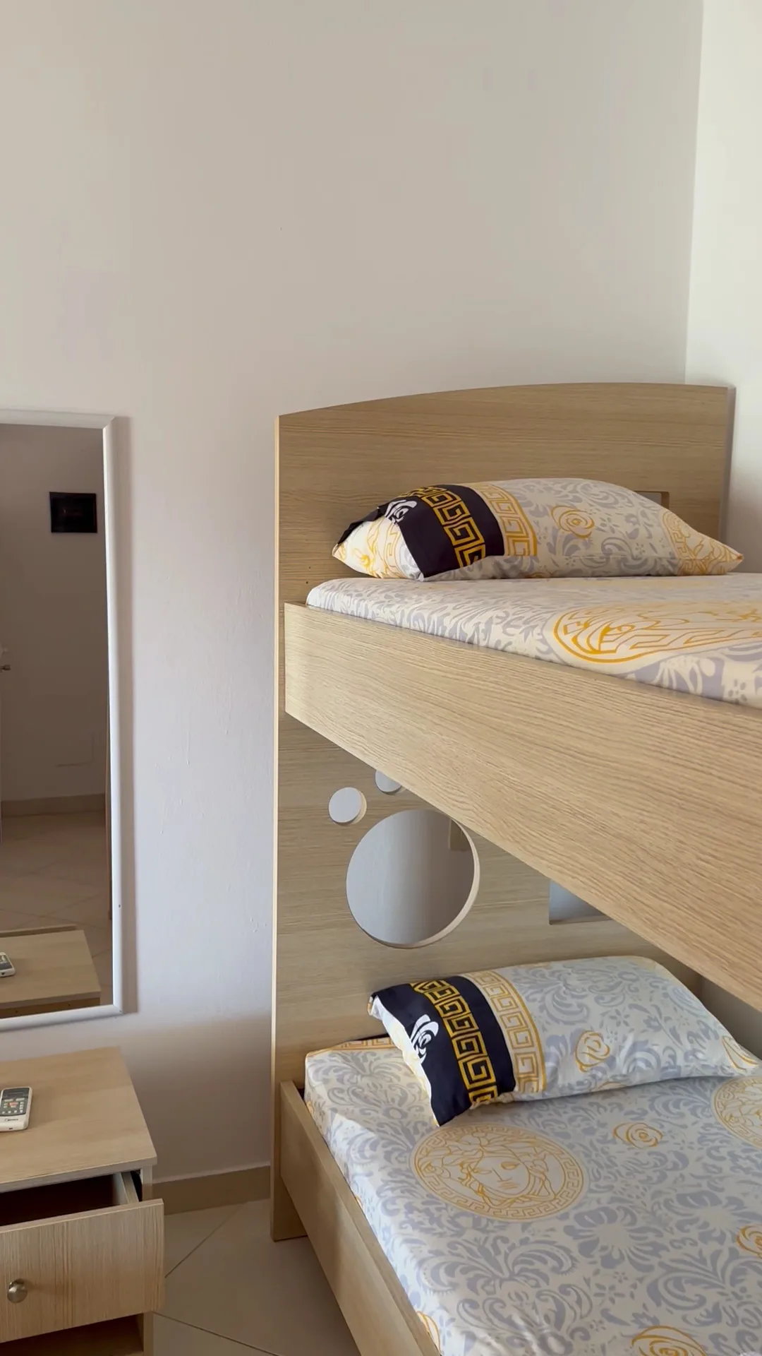 Pale oak bunk beds with patterned bedding beside a wall mirror and a bedside table