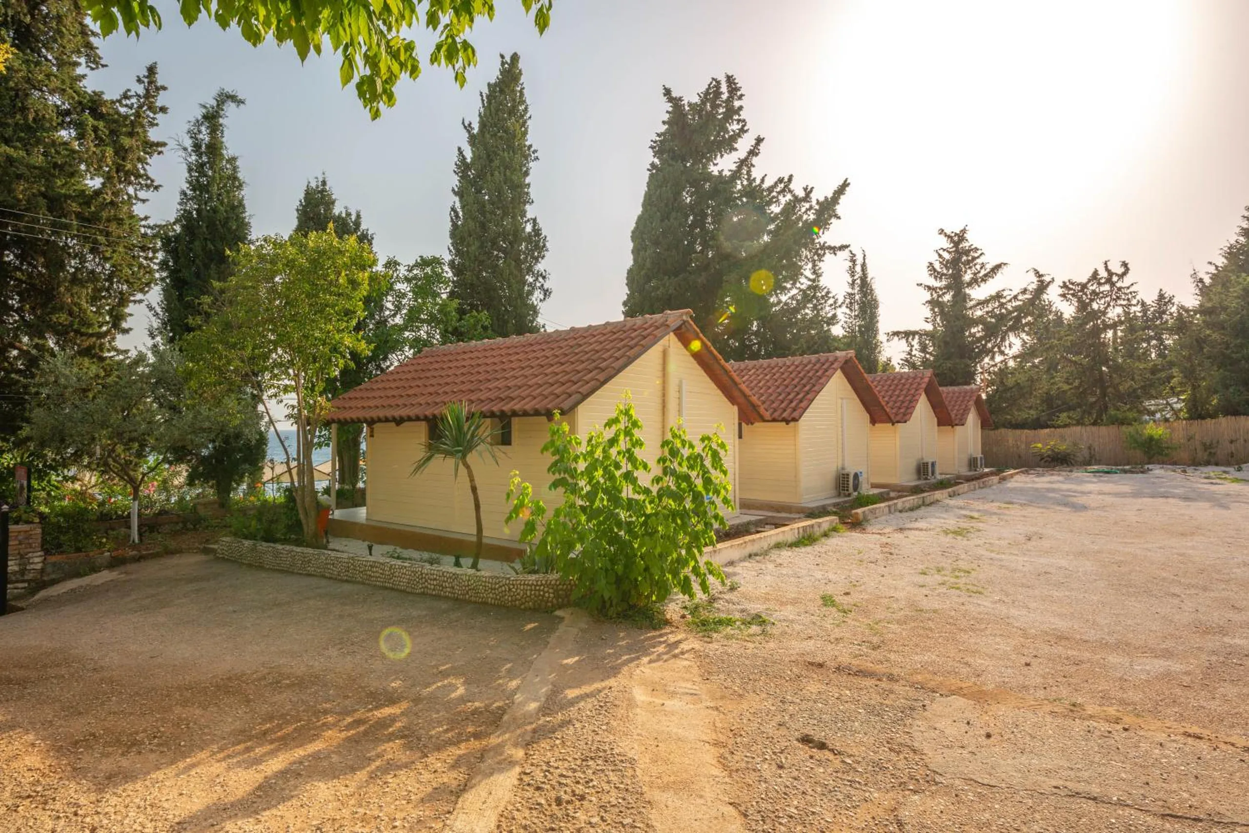 A gravel yard in front of the row of cream bungalows, cypress and olive trees around it