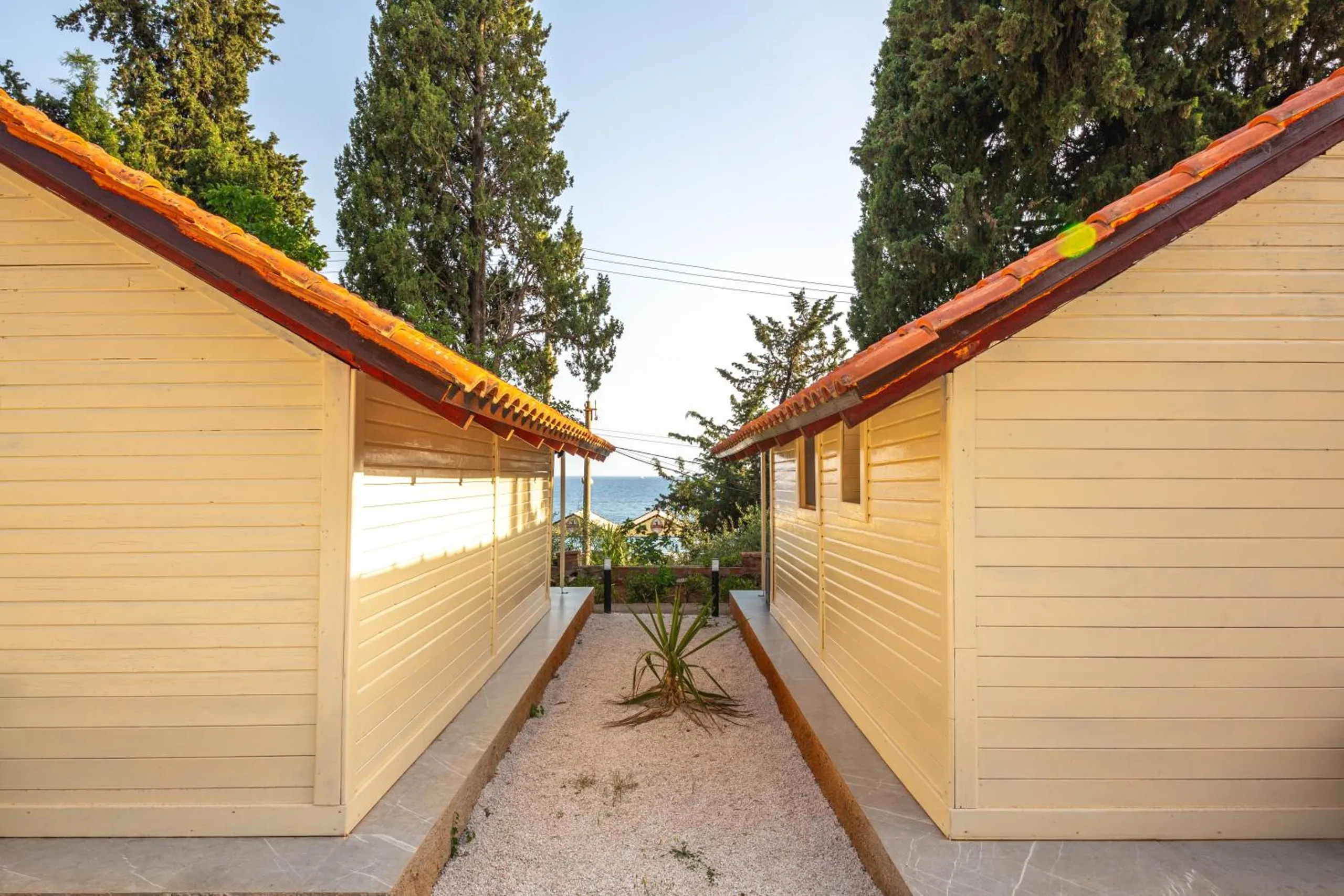A narrow path between two cream bungalows with pantile eaves, framing a slot of sea at the end