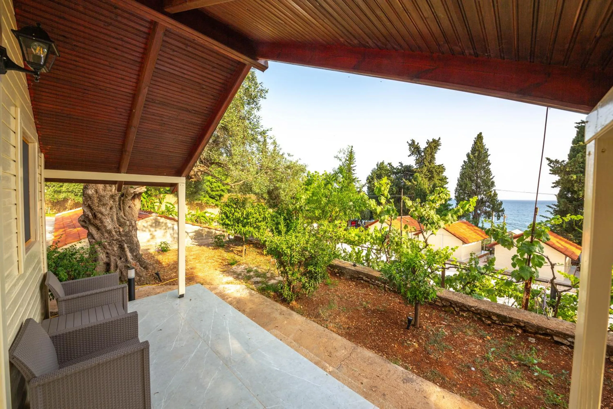 From a bungalow porch with two wicker chairs, the view over a planted garden and the roofs below to the sea