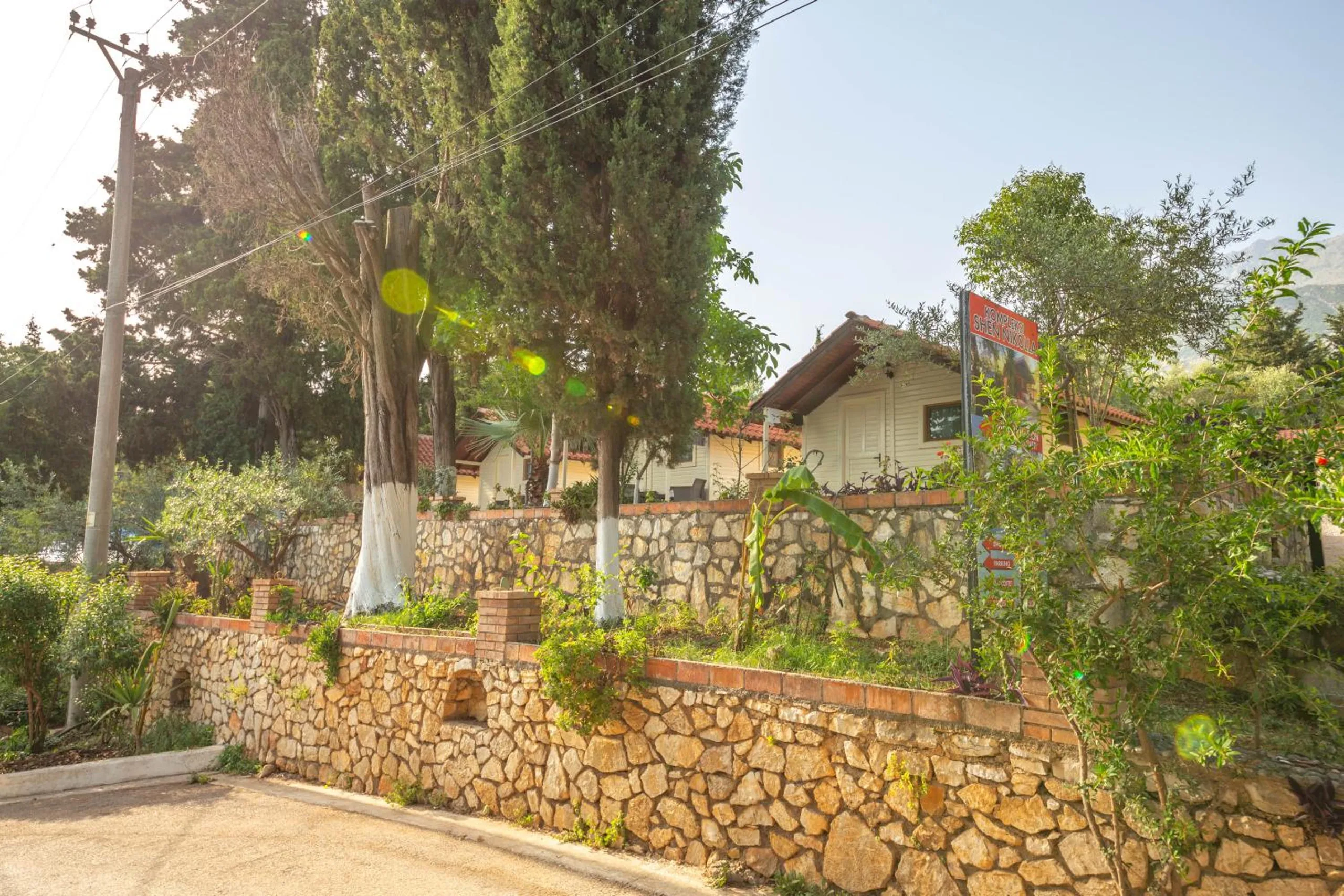 Dry-stone terrace walls planted with shrubs, a bungalow and a red sign at the top among white-limed trees