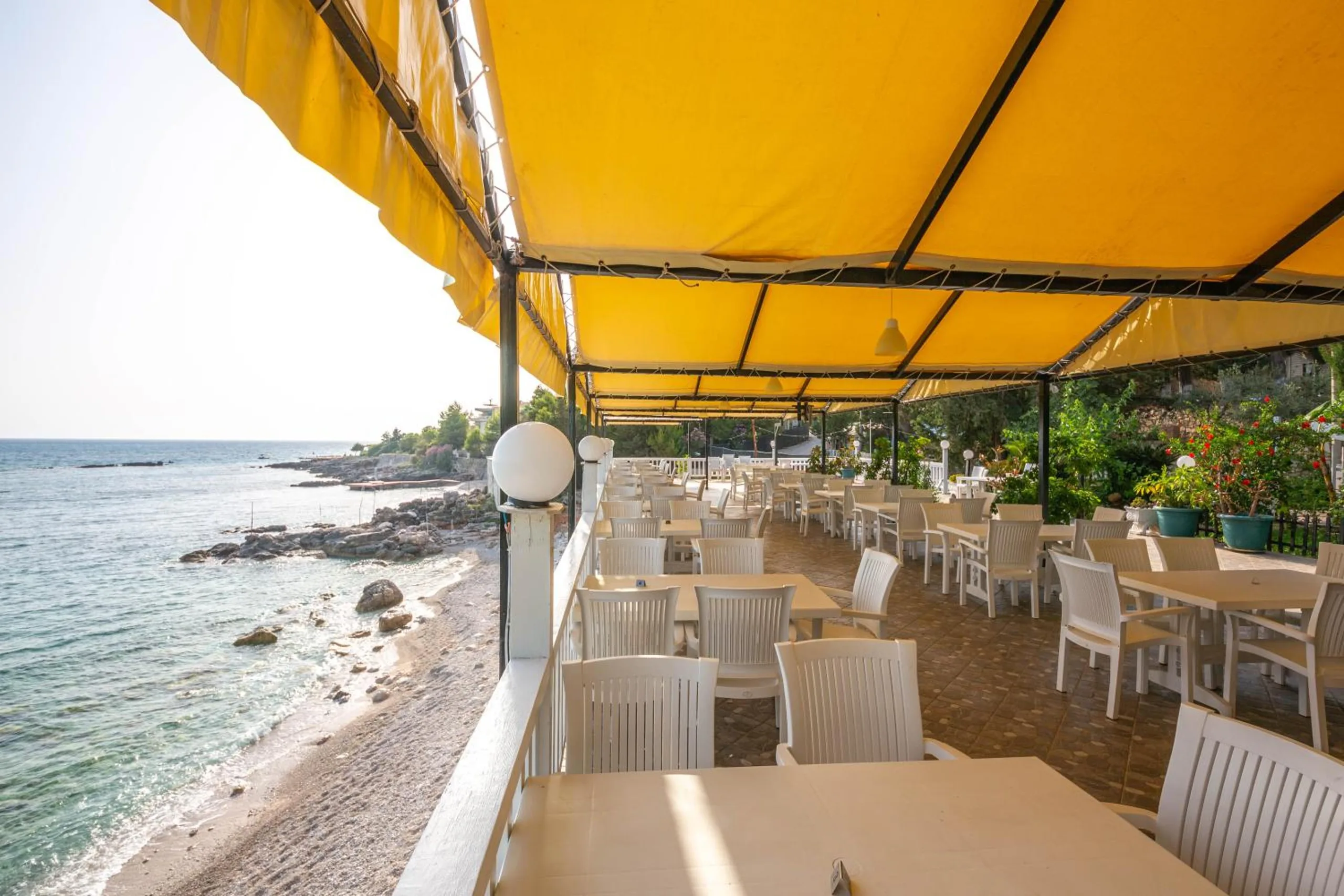 The restaurant deck seen from its far end, flowers along the rail and the shingle and rocks of the beach running north below it