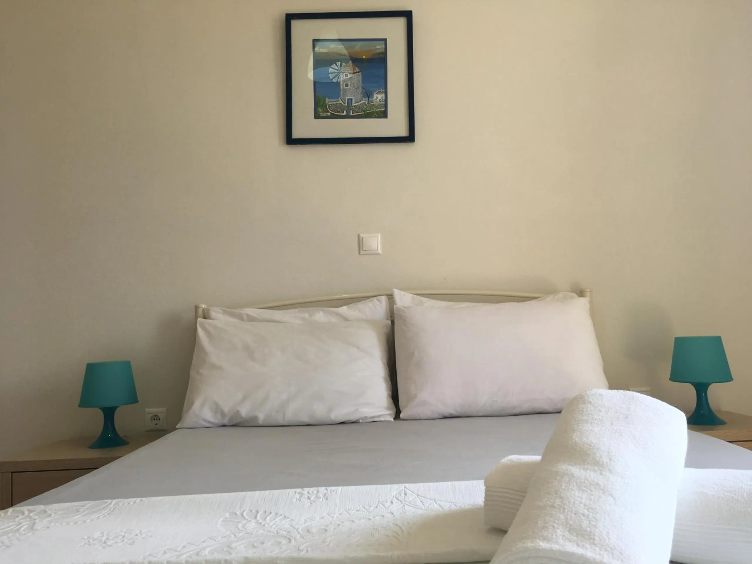 A made double bed between two turquoise bedside lamps, a framed print of a blue door above it