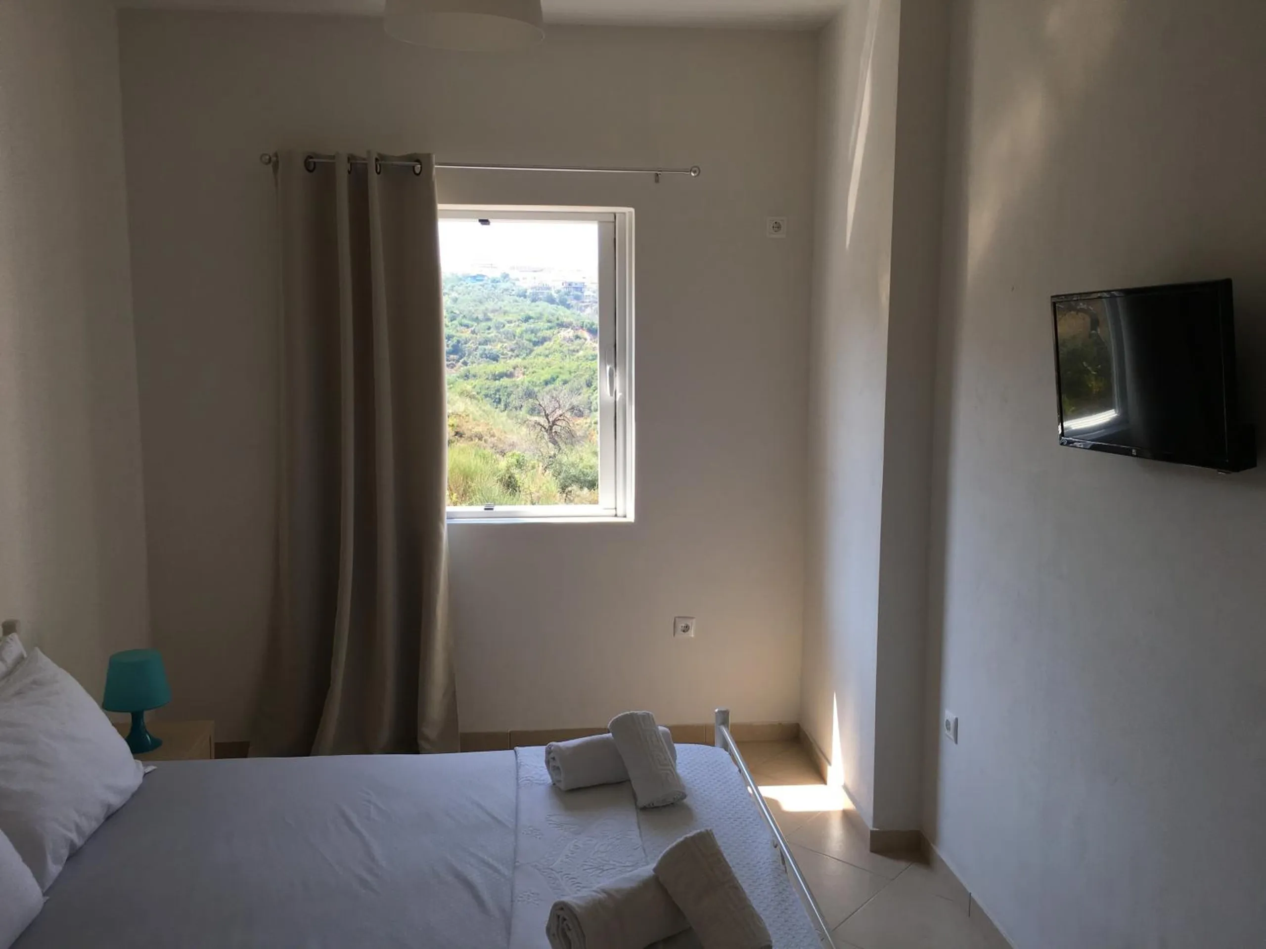 A double bed with towels laid out, a wall-mounted television and a window onto green hillside