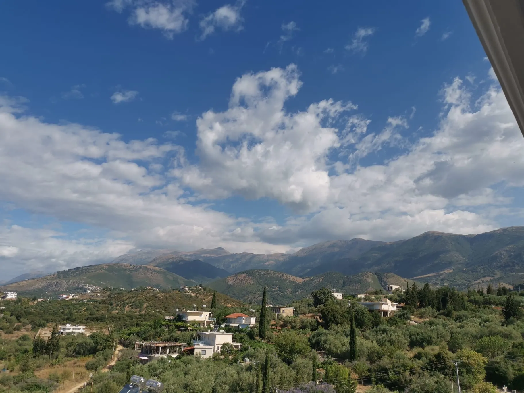 Inland from the balcony: green hills, cypresses and white houses below a long mountain ridge under cloud