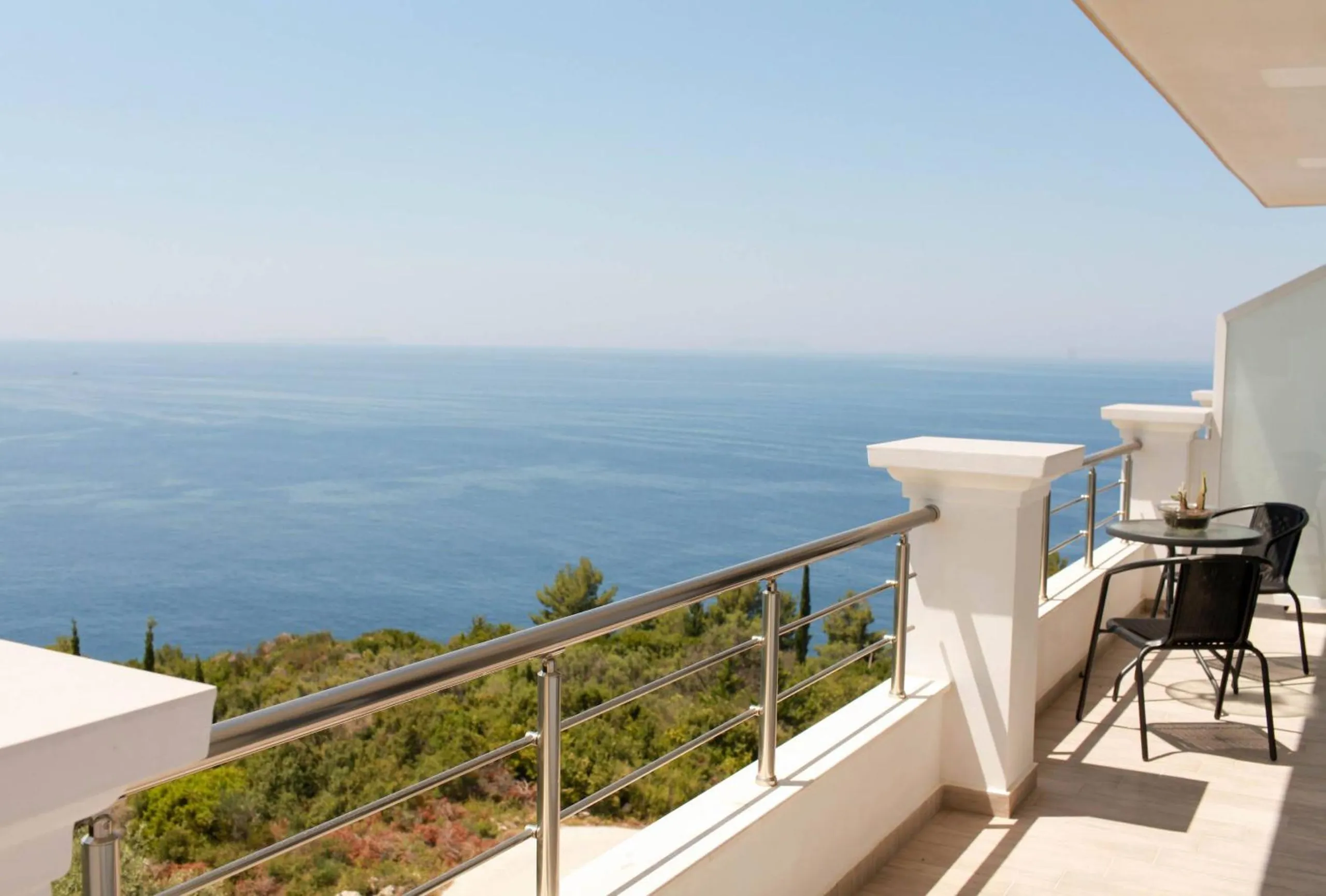 A long balcony with a stainless rail and a small table and chairs at the far end, the open sea filling the view