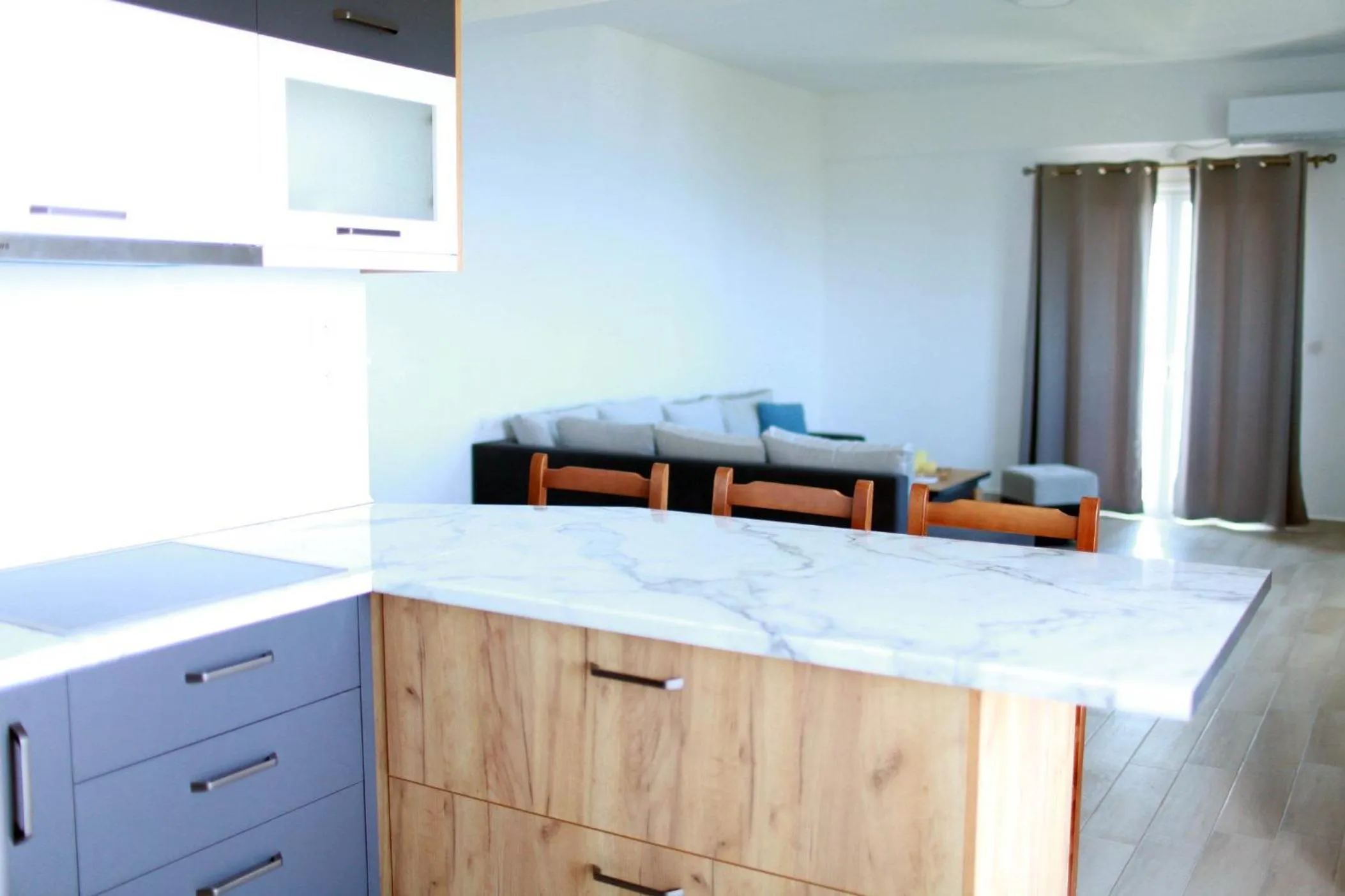 An open kitchen with a marble-effect counter, wood-fronted cupboards and a grey sofa beyond it