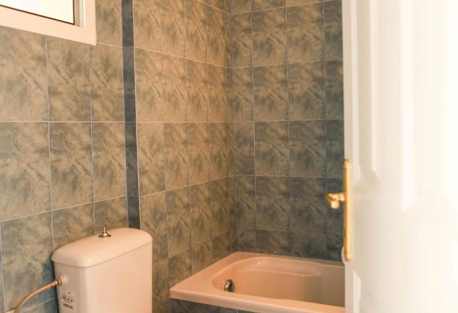 A tiled bathroom with a bathtub, a toilet and a white door